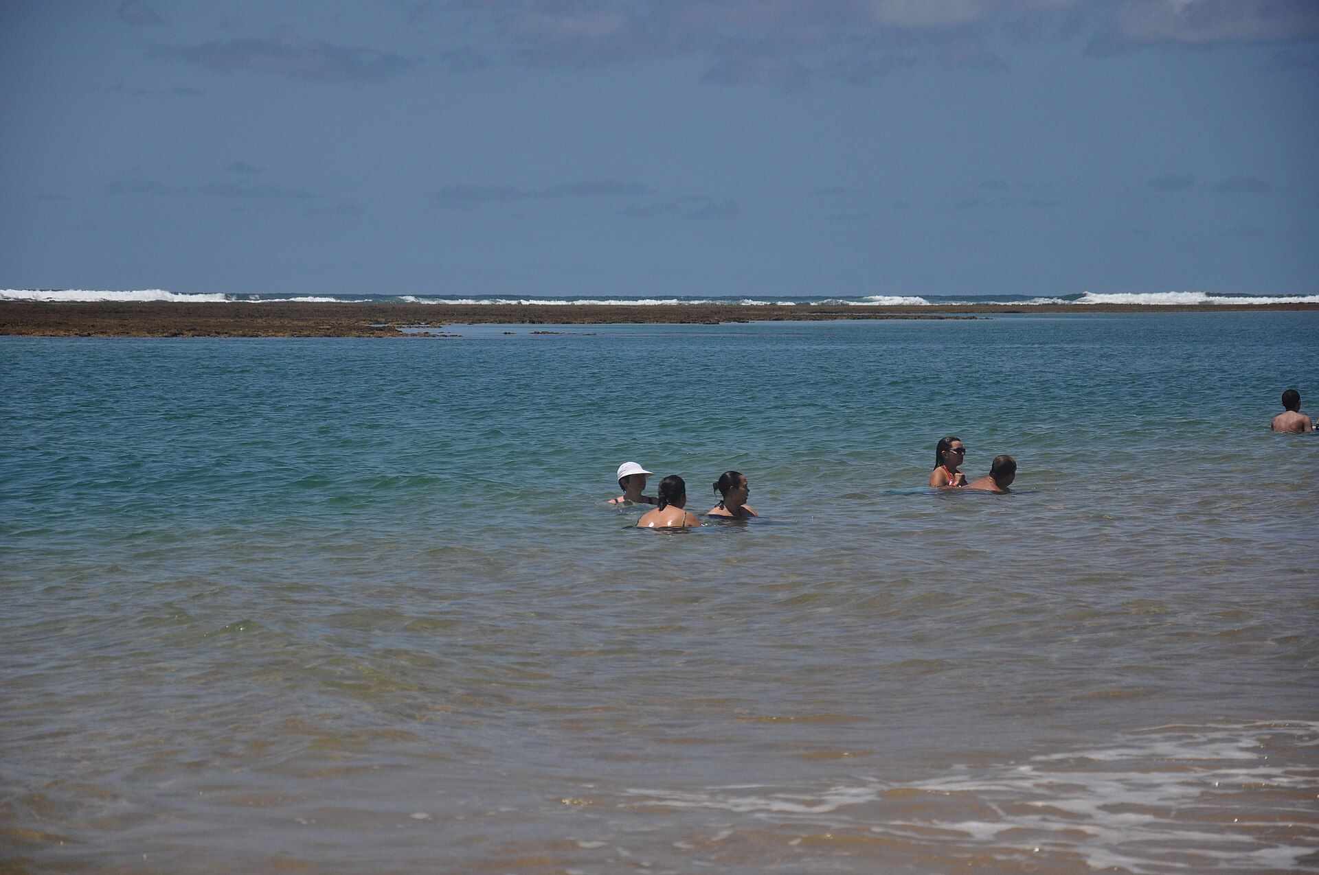 Banhistas nas piscinas naturais de Taipu de Fora, com a arrebentação no recife ao fundo